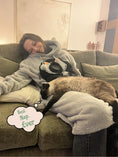 Load image into Gallery viewer, Woman lounging in a comfy wearable blanket hoodie with cat pocket, enjoying a cozy day at home.
